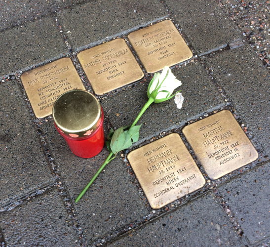 Photo of 5 „Stolpersteinen“ (stumbling stones), where a candle and a white rose were lied down.