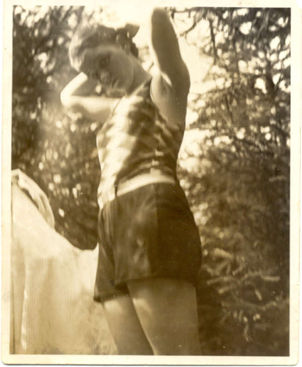 Old photograph of a young woman in summer clothes in front of trees.