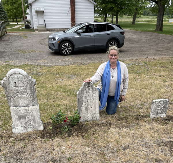 Andrea Bentschneider kneels next to the gravestone of her great-great-great-great-grandfather in a US cemetery.