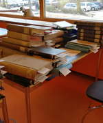 Photo of a desk stacked full of books and files in the State Archive Hamburg reading room.